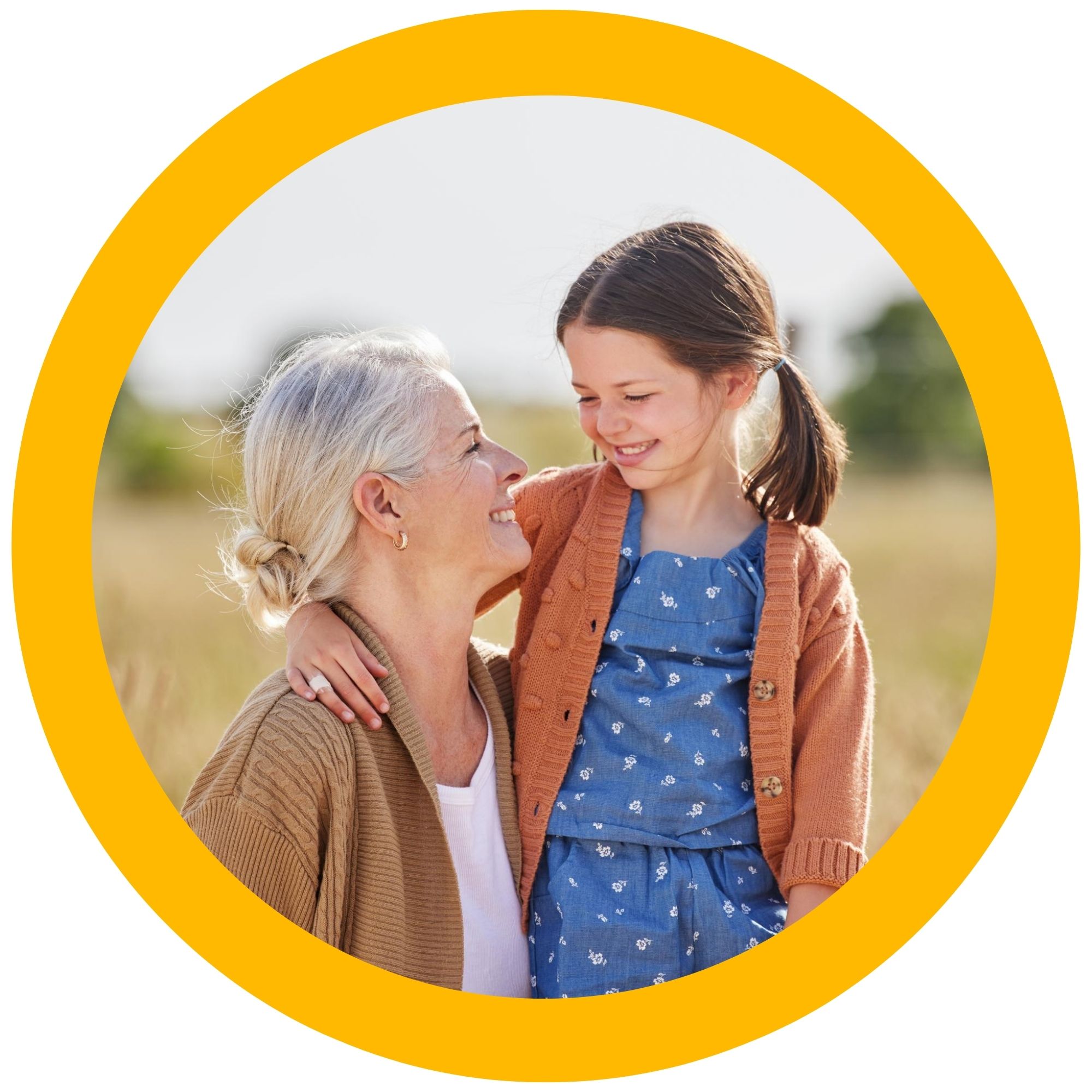 An elderly woman, sitting, looks up at a young girl who's looking back at her, both smiling. The image is in a yellow circle.