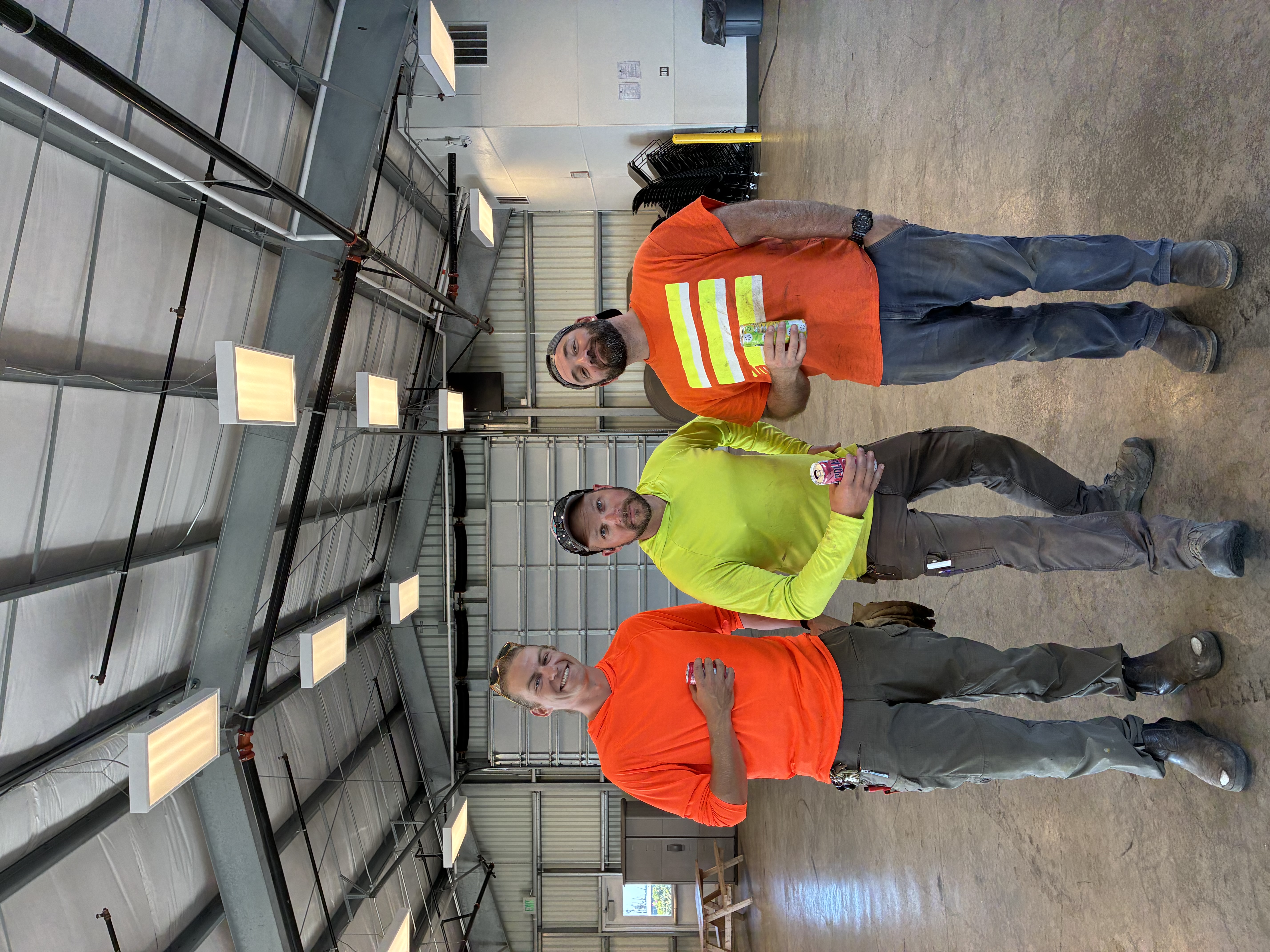 Three Port of Bellingham employees in reflective orange and yellow shirts pose for a picture while waiting for their cars to get washed.